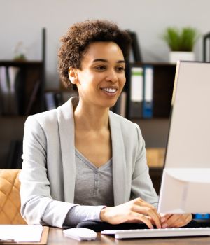 A woman typing on her computer and smiling as she takes part in an online environmental or safety training course