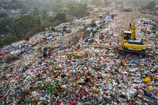 A digger atop a huge landfill, with plastic and other waste as far as the eye can see