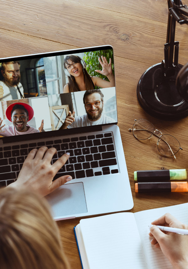 A person working on their laptop writing notes, and the laptop has a Zoom call open with four other people attending from across the world