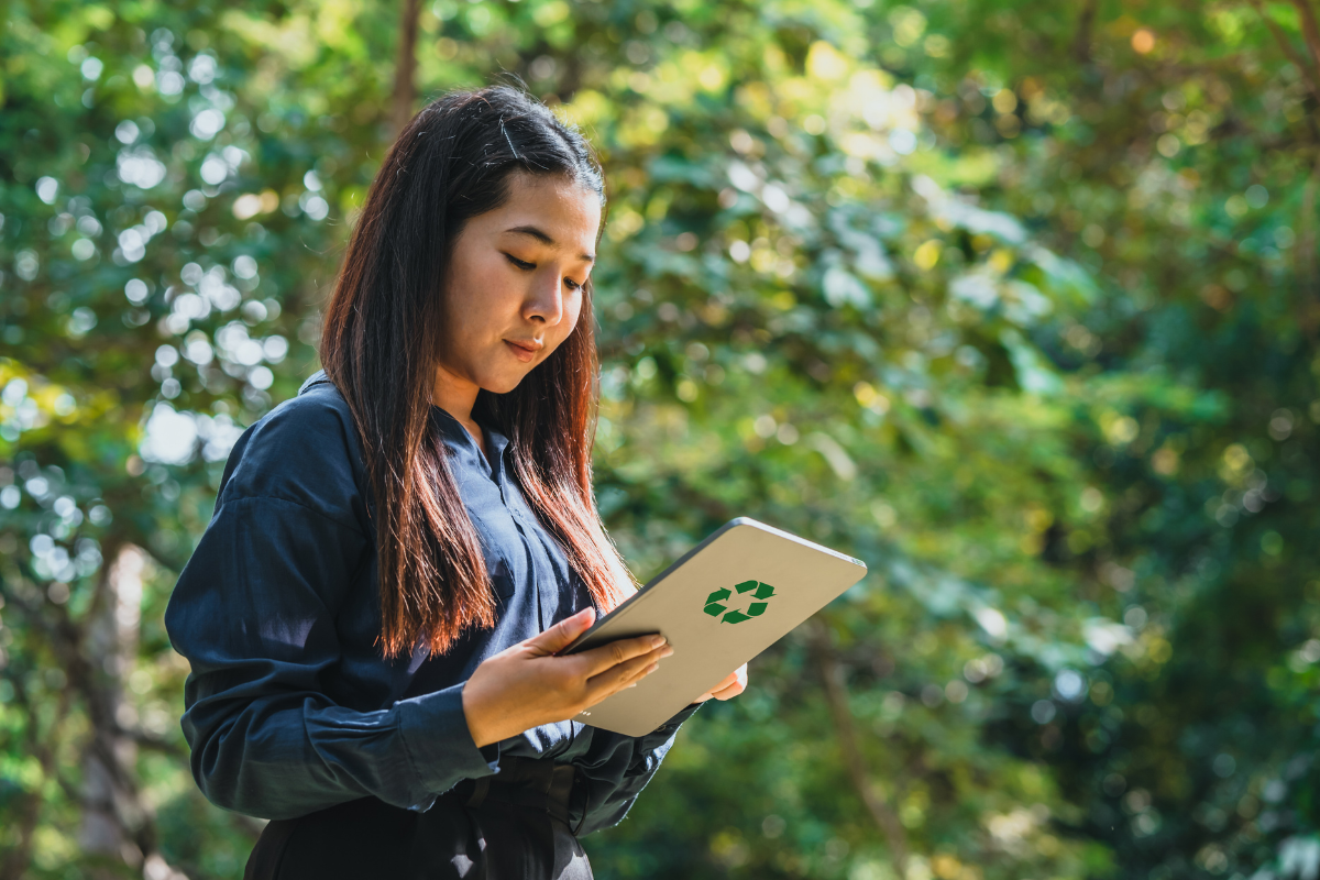 Women stood among nature looking on tablet with recycling sign