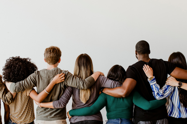 A row of diverse people facing away from the camera, all in a line with their arms around each other's waists
