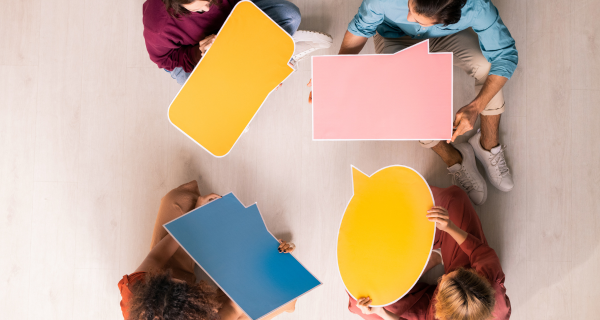 Four people sitting together on a table holding different speech bubbles