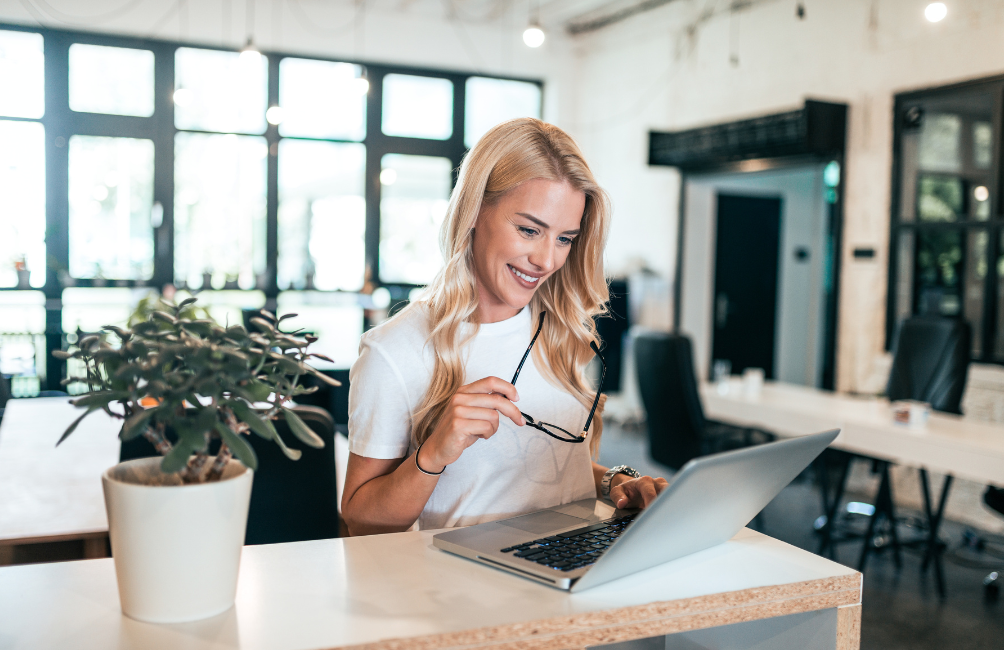 Woman with glasses in hand working on laptop