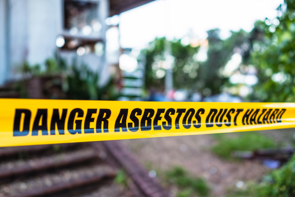 Yellow hazard tape stretched in front of a property which reads, "DANGER ASBESTOS DUST HAZARD"