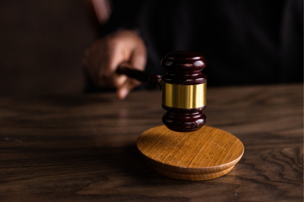 A hand hitting a dark wooden gavel on a wooden desk