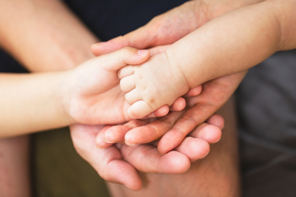 A close up of parents' hands holding a baby's hand
