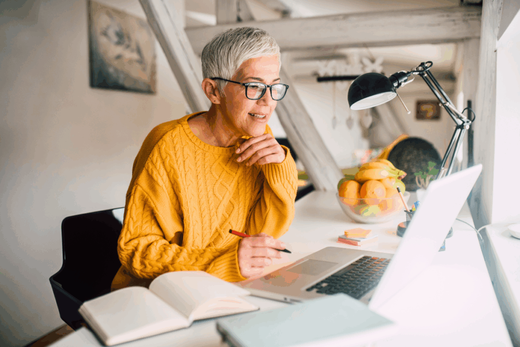 A lady with an orange jumper on working from home with a laptop and pen