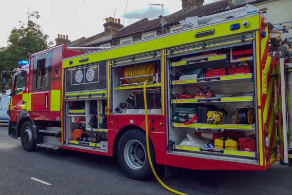A British fire engine parked with all side doors open, showing the fire hose.