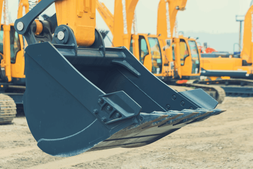 Grey excavator bucket with other yellow excavators in the background