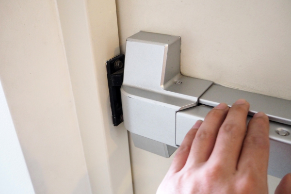 A close up of a hand pushing on the bar of a fire exit door