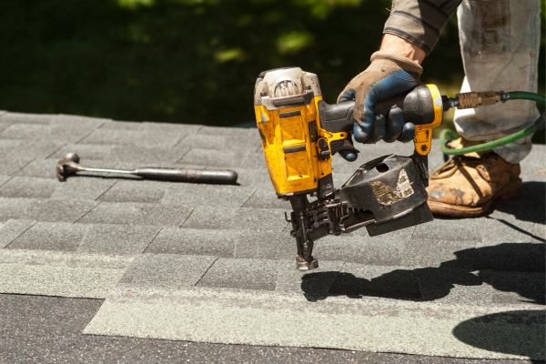Roofers replacing old roof shingles with new shingles on a residential home using a nail gun