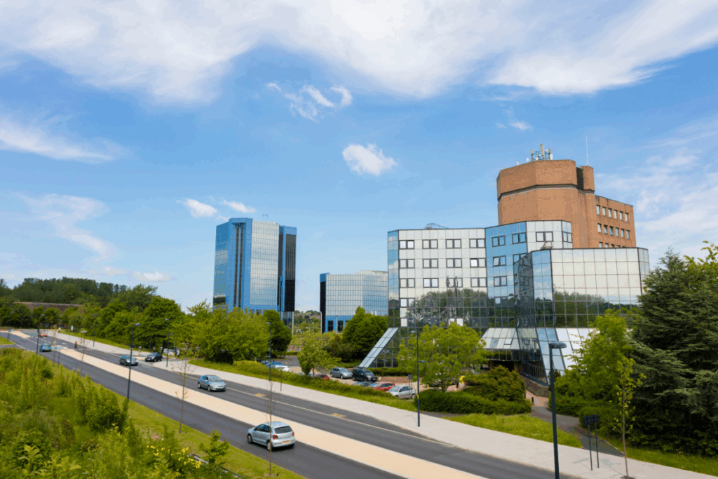A blue sky and clouds with tall buildings and a long road with cars on
