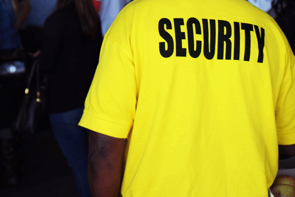 A door supervisor with a yellow t-shirt that says security on the back with a public venue background