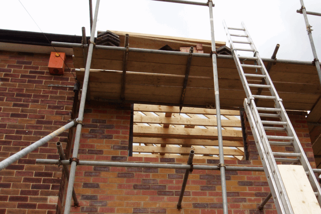 Red brick house extension with ladder and wood, with a grey sky
