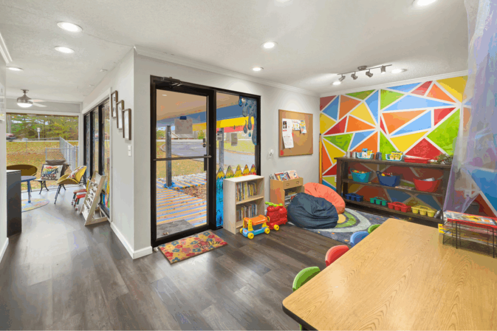 Toddler room with white walls and bright wall art and large doors, and colourful chairs