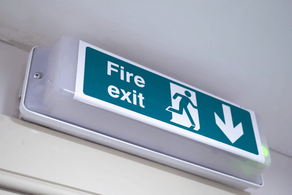 Fire door sign on top of a wall near the ceiling that says fire exit in white text with green background