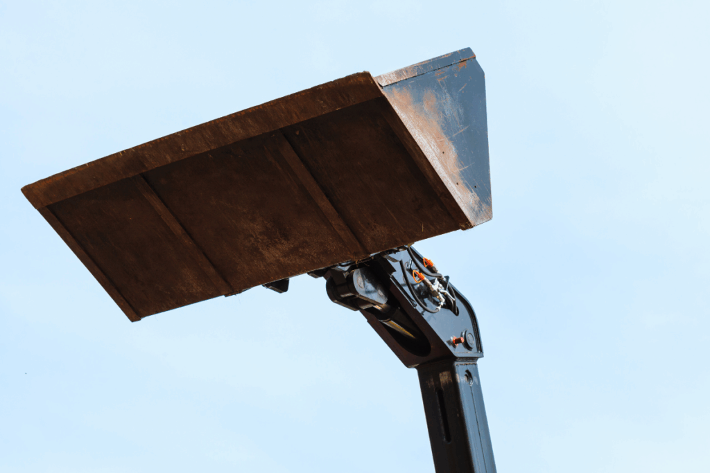A loading bucket lifted upwards by machinery and a blue sky in the background