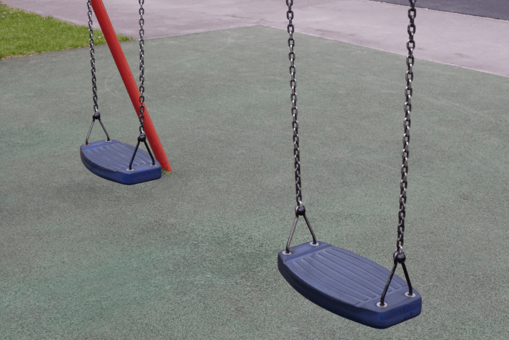 Astroturf green-floored playground with two swings with dark blue rubber seats and black metal chains