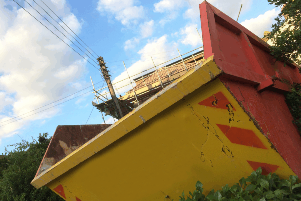 Yellow and red skip close up with a building and the sky in the background