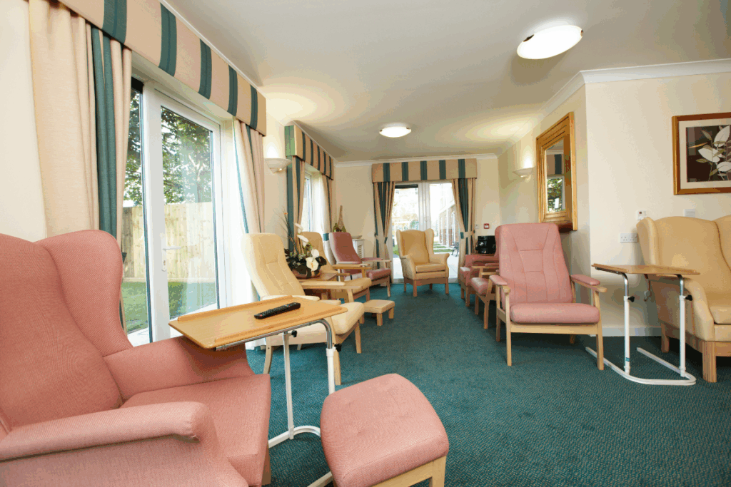 Main room of a care home with pink material seats and wooden tables and dark green carpet