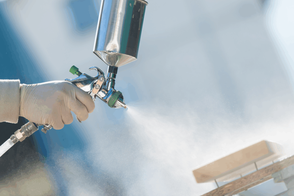 A person completing industrial spray painting with silver metal equipment and white paint spraying onto materials