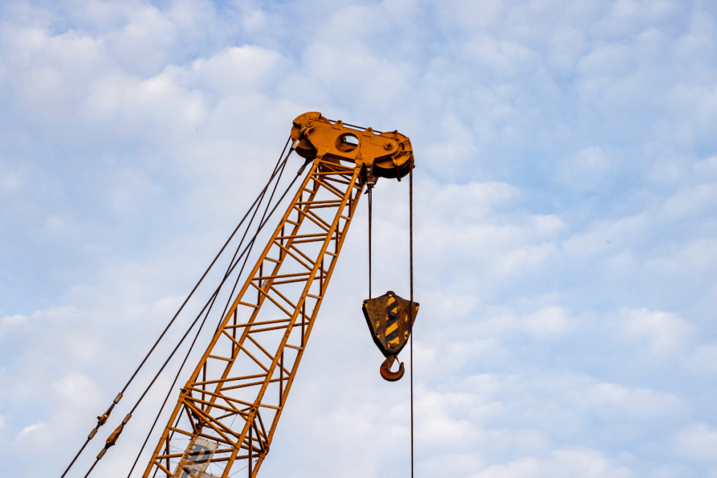 Yellow and black metal crane with strong wiring to support the lifting of heavy loads, with blue sky and white clouds behind it.
