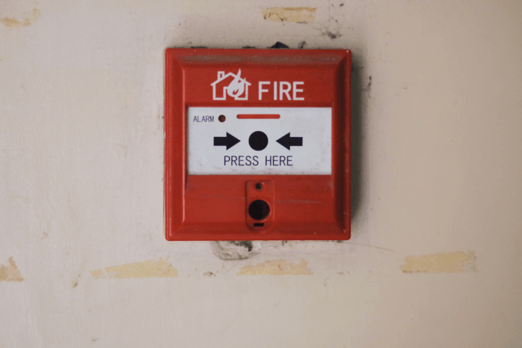 Red, white and black fire alarm on a wall with cracked cream paint and plaster showing