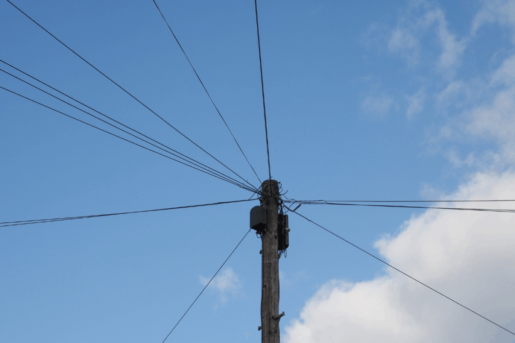 Wooden telecommunications pole with wires leaving the pole in different directions and blue sky and clouds