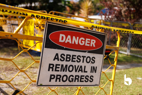 A yellow chain link fence with a sign on it saying "DANGER: Asbestos Removal In Progress"