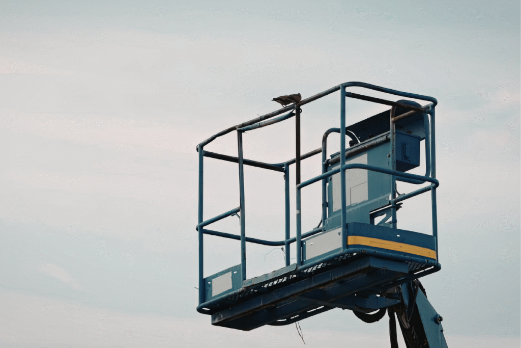 A dark grey mobile elevating work platform (MEWP) in the air with grey and white sky behind it