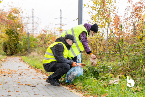 Two people in hi-vis jackets cleaning up waste and litter from a green area
