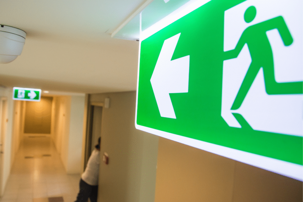 Green and white fire exit safety sign in a corridor with a light shining on it to amplify it