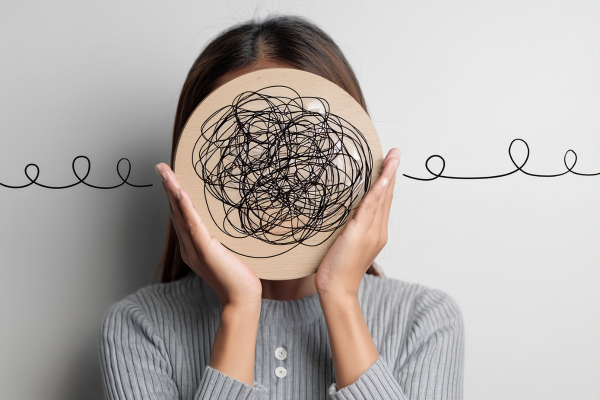 A photo of a woman holding up a big scribble in front of her face, representing challenging mental health