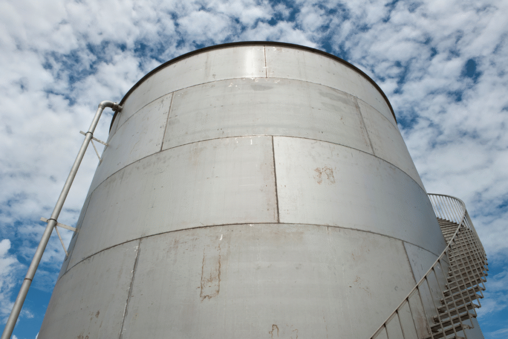 large metal storage tank with blue sky and clouds behind it