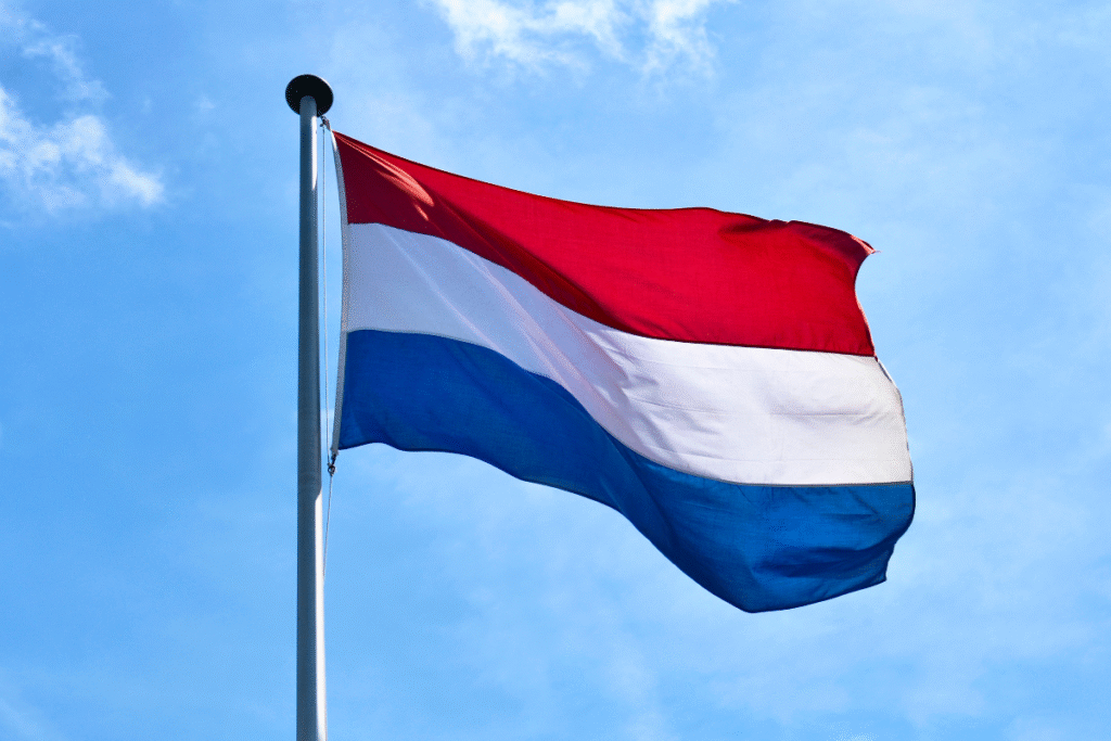 The Dutch flag in the air with blue sky behind it