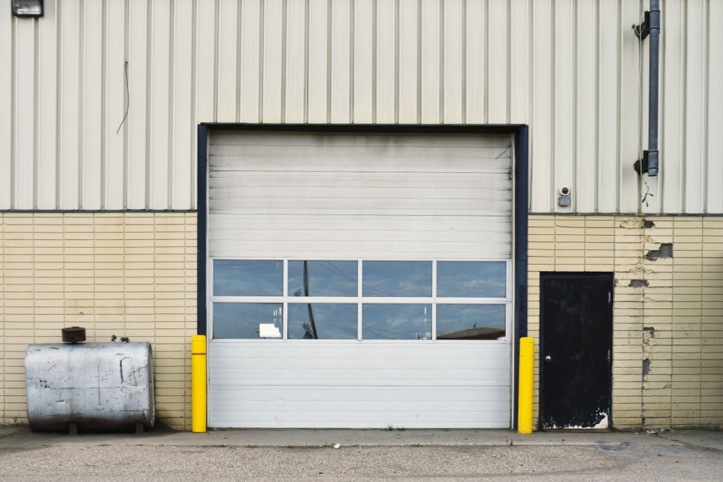 An industrial overhead door closed with yellow structures either side and glass windows