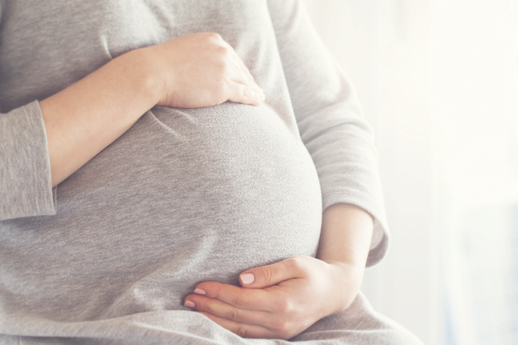 A pregnant woman with a grey jumper on holding her stomach