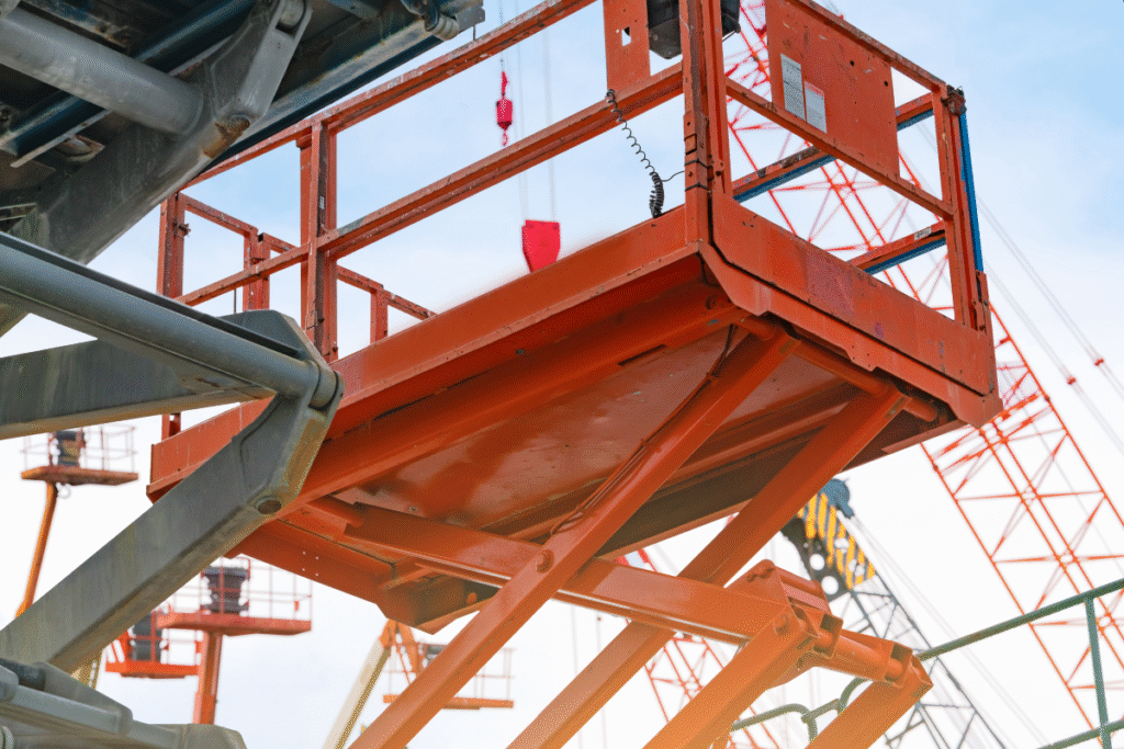 An orange scissor lift in the air next to a building