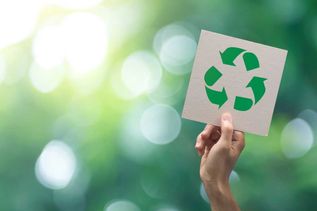 A hand holding a piece of paper with a recycling symbol on