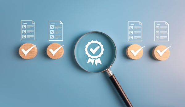 Icons of documents with check marks on top of them, with a magnifying glass highlighting an achieved certification rosette
